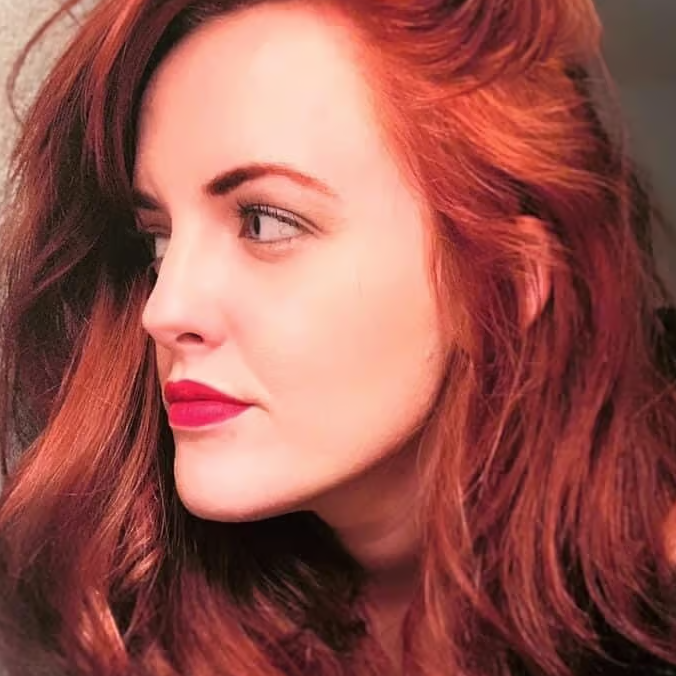 Profile view of a woman with long red hair and red lipstick, looking to the side.
